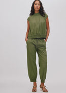 A woman modelling a matching olive green two-piece set consisting of a short-sleeve cropped top and relaxed drawstring pants, paired with brown heeled sandals, against a light grey studio background.