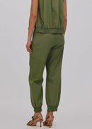 A woman shown from the back wearing an olive green sleeveless top and matching jogger pants, paired with brown heeled sandals, against a light gray studio background.
