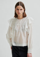 Woman wearing a white blouse with ruffled sleeves on a plain background