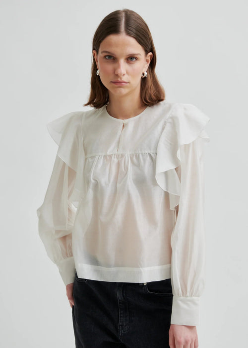 Woman wearing a white blouse with ruffled sleeves on a plain background