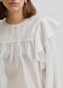 Woman wearing a white blouse with ruffled sleeves on a plain background