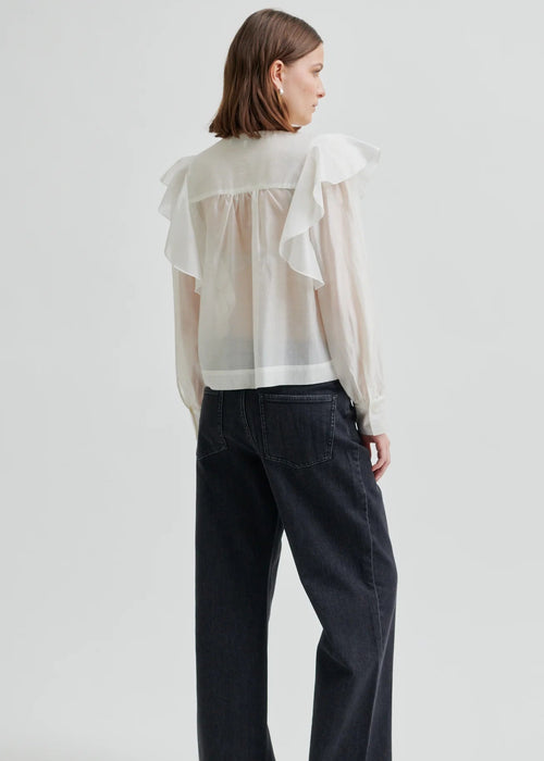 Woman wearing a white blouse with ruffled sleeves on a plain background