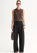 A model stands against a plain light background wearing a brown sleeveless button-front knit top,