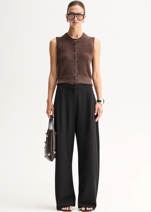 A model stands against a plain light background wearing a brown sleeveless button-front knit top,