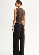 A model stands against a plain light background wearing a brown sleeveless button-front knit top,