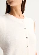 Close-up of a model wearing a fuzzy white sleeveless top with a vertical row of silver buttons down the front, paired with a small silver hoop earring.