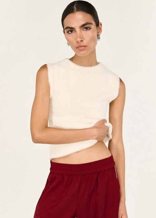 Woman wearing a white sleeveless top and red pants on a beige background