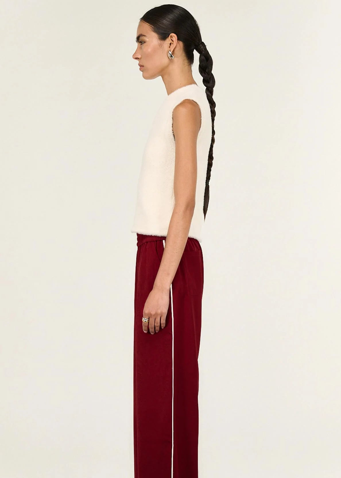 Woman wearing a white sleeveless top and red pants on a beige background