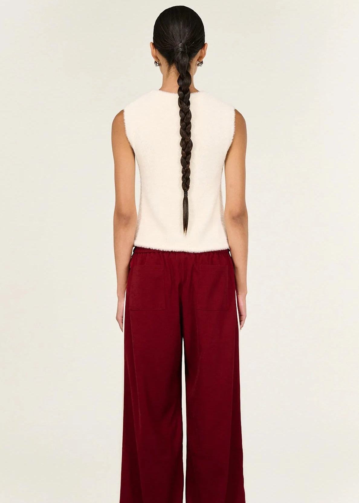 Woman wearing a white sleeveless top and red pants on a beige background