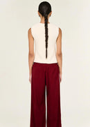 Woman wearing a white sleeveless top and red pants on a beige background
