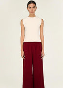 Woman wearing a white sleeveless top and red pants on a beige background