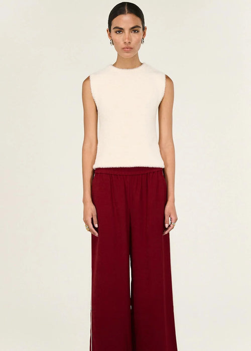 Woman wearing a white sleeveless top and red pants on a beige background