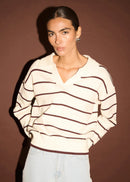 Woman wearing a striped sweater and light blue jeans against a brown background