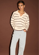 Woman wearing a striped sweater and light blue jeans against a brown background
