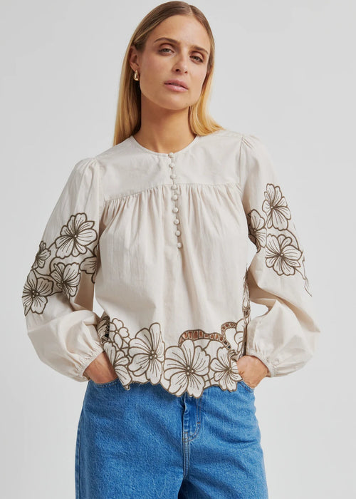 Woman wearing a white blouse with floral embroidery and blue jeans on a white background