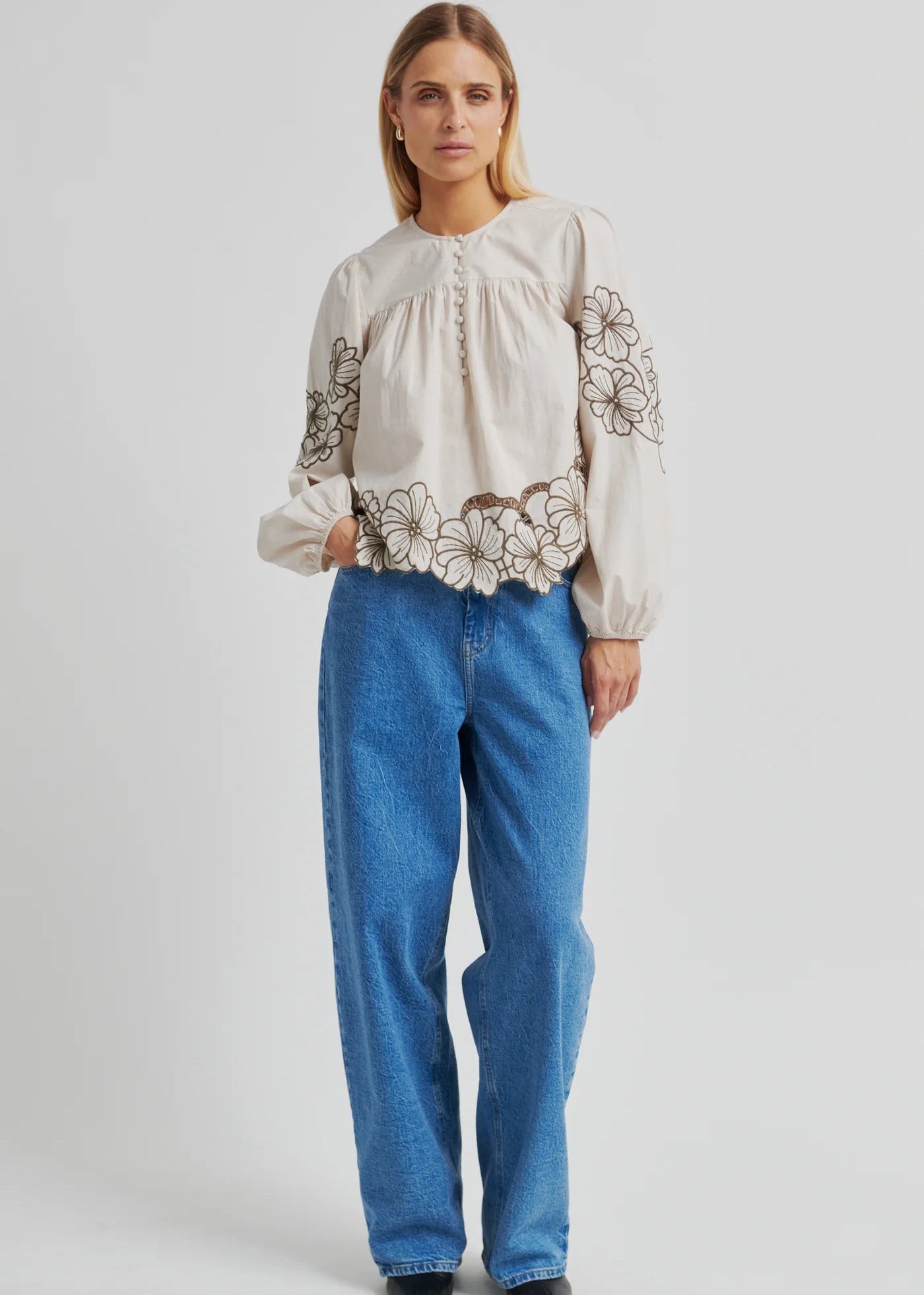 Woman wearing a white blouse with floral embroidery and blue jeans on a white background
