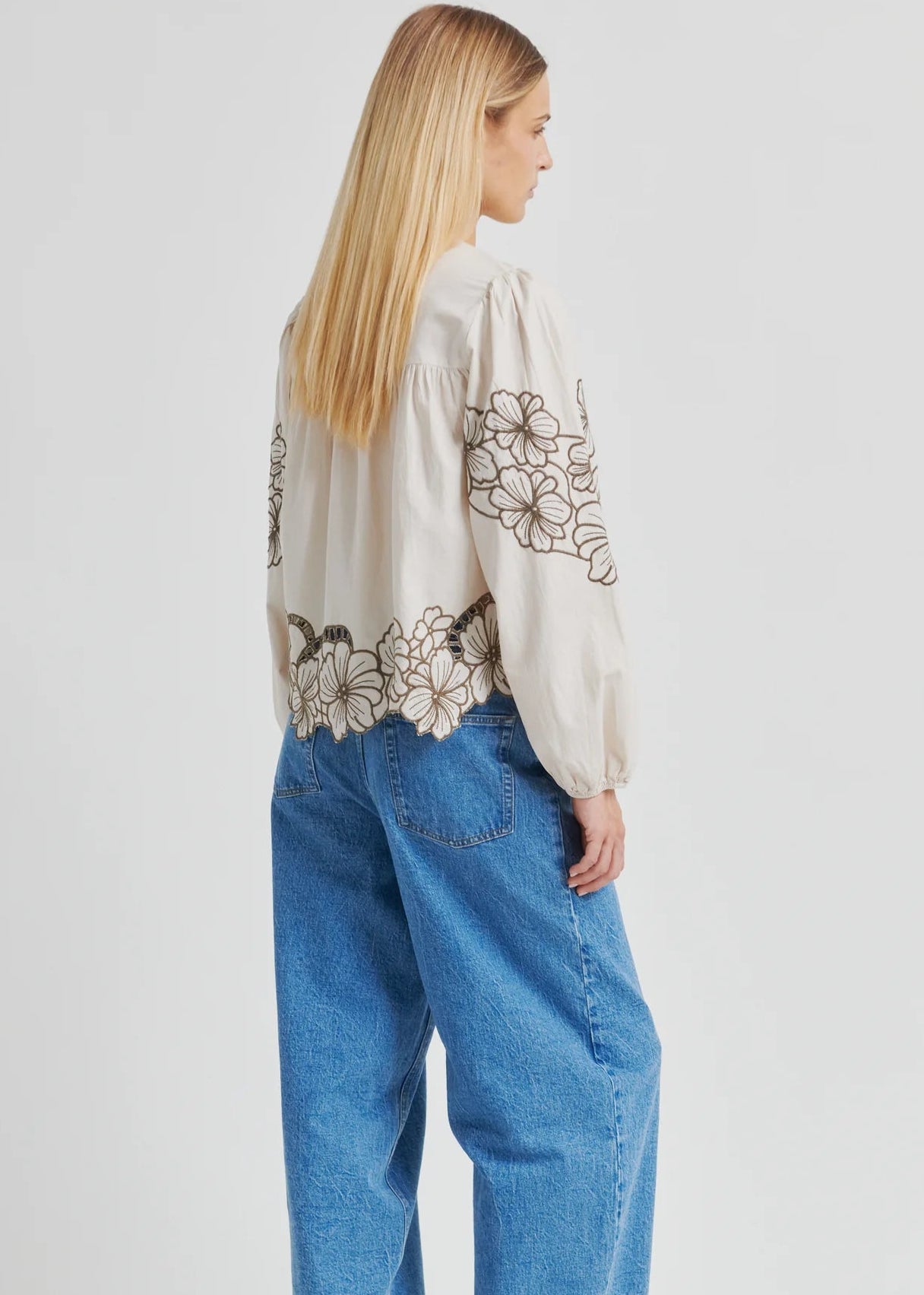Woman wearing a white blouse with floral embroidery and blue jeans on a white background