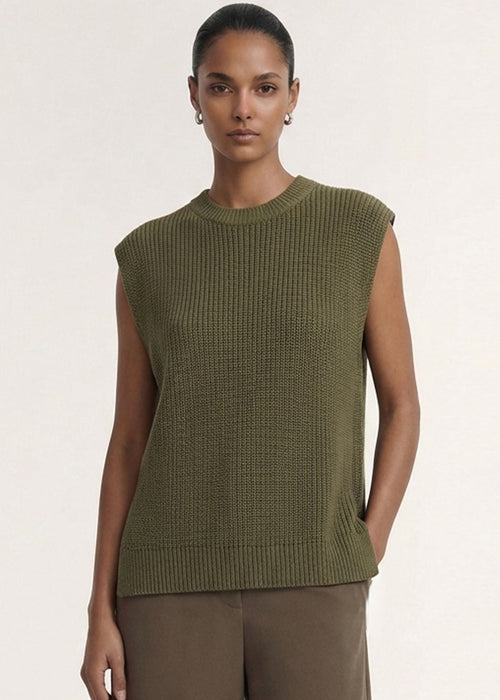 A model wearing an olive green ribbed sleeveless knit top and brown wide-leg trousers, standing against a plain off-white studio background.