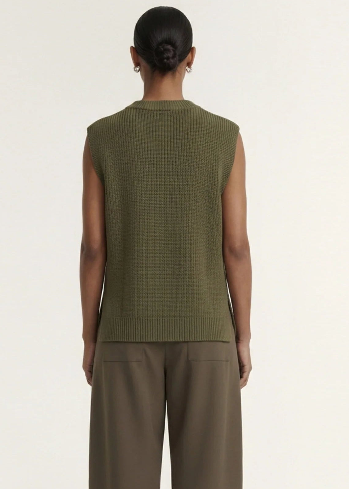 A model wearing an olive green ribbed sleeveless knit top and brown wide-leg trousers, standing against a plain off-white studio background.