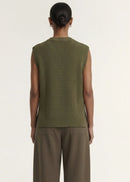 A model wearing an olive green ribbed sleeveless knit top and brown wide-leg trousers, standing against a plain off-white studio background.