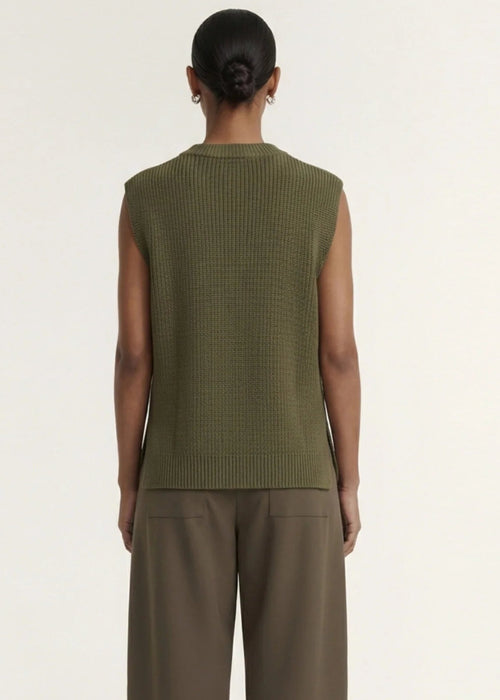 A model wearing an olive green ribbed sleeveless knit top and brown wide-leg trousers, standing against a plain off-white studio background.