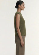 A model wearing an olive green ribbed sleeveless knit top and brown wide-leg trousers, standing against a plain off-white studio background.