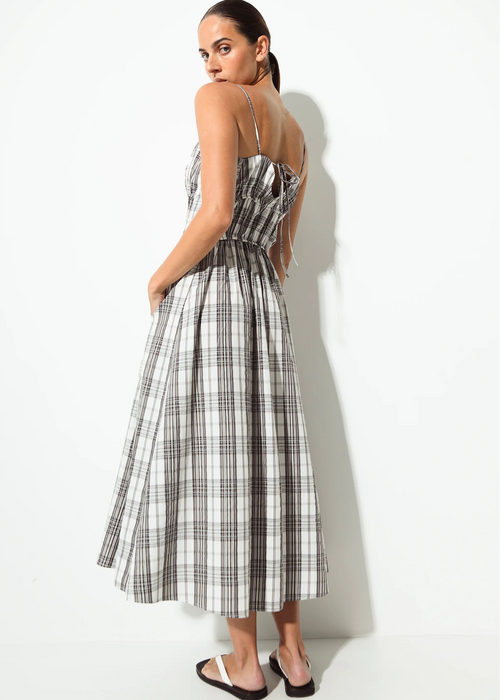 A woman modelling a sleeveless midi dress with a grey, white, and black plaid pattern, shown from a back-three-quarter angle against a plain white studio background.