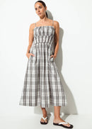 A woman modelling a sleeveless midi dress with a grey, white, and black plaid pattern, shown from a back-three-quarter angle against a plain white studio background.