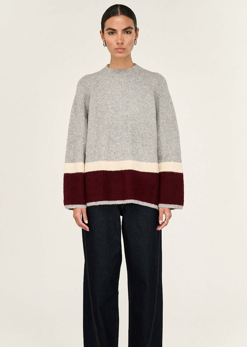 Woman wearing a grey sweater with a colour-blocked design on a white background
