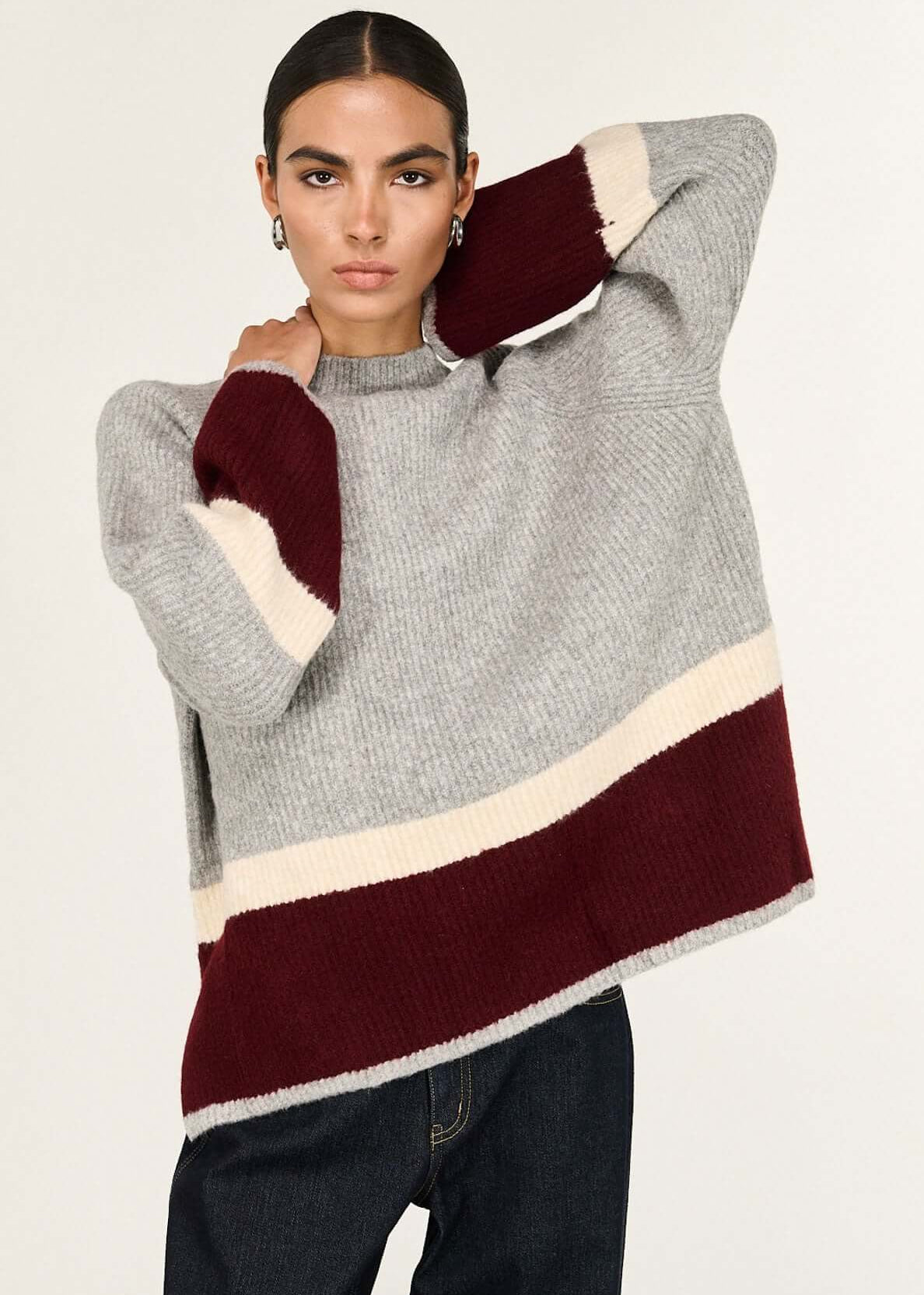 Woman wearing a grey sweater with a colour-blocked design on a white background