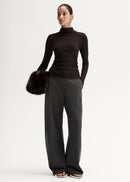 Woman wearing a black turtleneck and grey pants on a white background