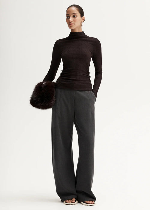 Woman wearing a black turtleneck and grey pants on a white background
