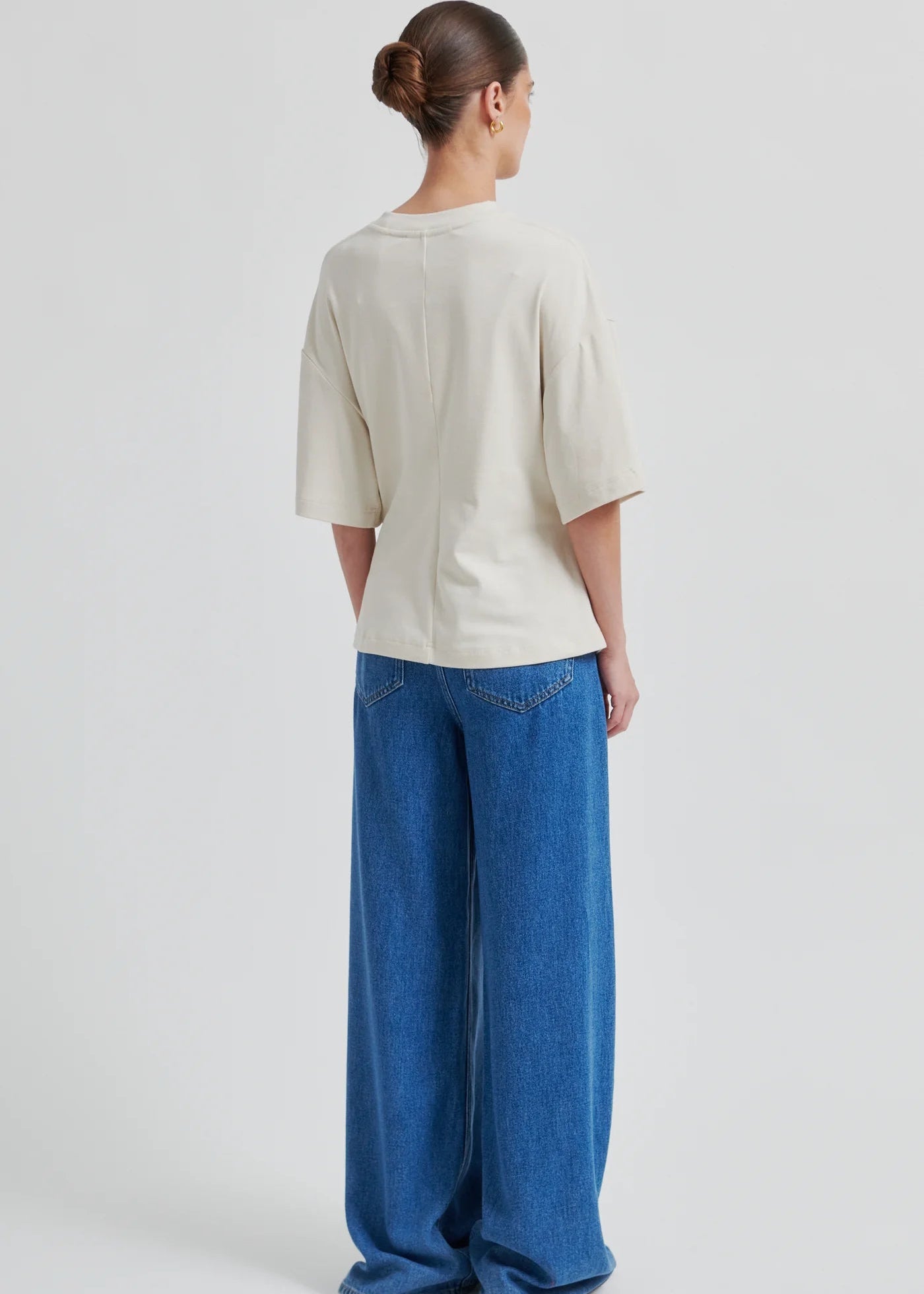 Woman wearing a cream-colored top with a brooch and blue jeans on a white background