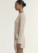A model wearing a long-sleeve, wrap-style mini dress with a delicate beige and white floral print, set against a plain off-white studio background.