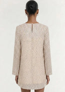 A model wearing a long-sleeve, wrap-style mini dress with a delicate beige and white floral print, set against a plain off-white studio background.