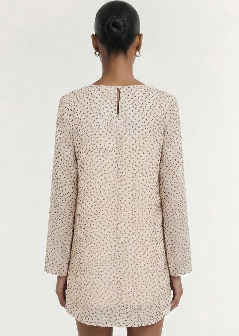 A model wearing a long-sleeve, wrap-style mini dress with a delicate beige and white floral print, set against a plain off-white studio background.