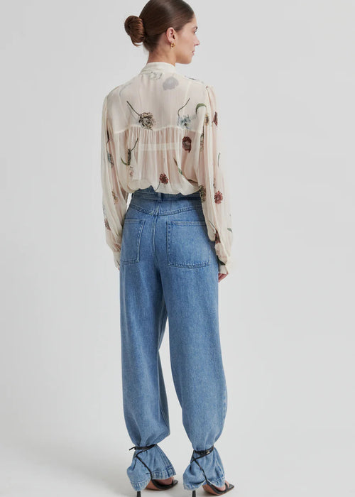 Woman wearing a floral blouse and blue jeans on a white background