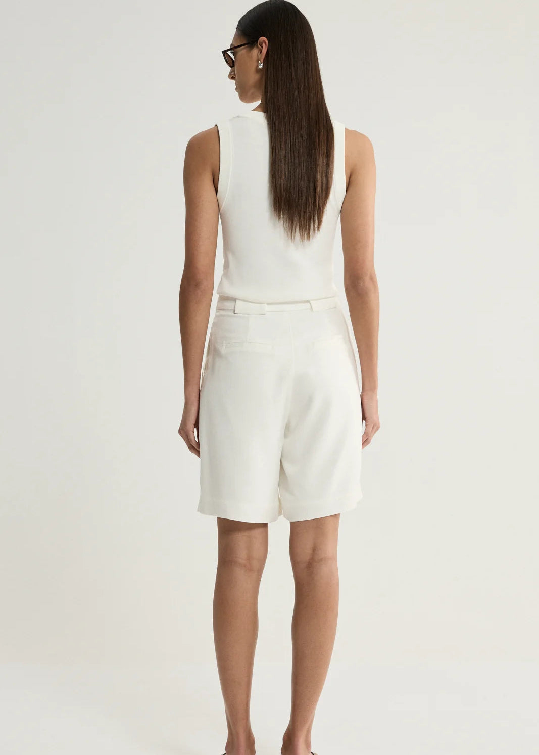 A woman is shown from behind wearing a white sleeveless top and matching white shorts against a plain light background.