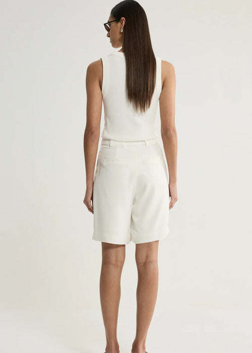 A woman is shown from behind wearing a white sleeveless top and matching white shorts against a plain light background.