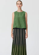 A model stands against a light grey studio background wearing a sleeveless olive green top and a long pleated skirt with vertical cream, black, and green stripes