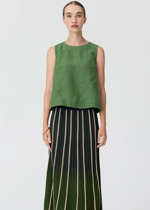 A model stands against a light grey studio background wearing a sleeveless olive green top and a long pleated skirt with vertical cream, black, and green stripes