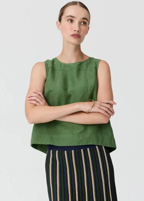 A model stands against a light grey studio background wearing a sleeveless olive green top and a long pleated skirt with vertical cream, black, and green stripes