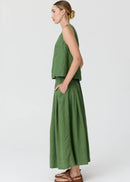 A woman modelling in profile a matching olive green two-piece linen set consisting of a sleeveless crop top and a high-waisted, wide-leg maxi skirt, paired with brown leather sandals against a light grey studio background.