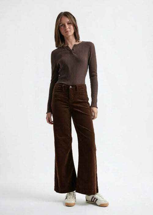 Woman wearing a brown long-sleeve top and brown velvet  pants on a white background