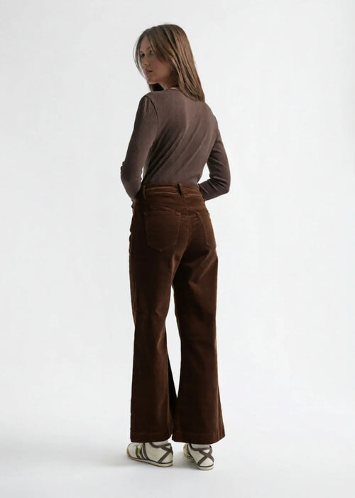 Woman wearing a brown long-sleeve top and brown velvet  pants on a white background