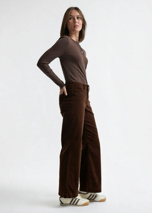 Woman wearing a brown long-sleeve top and brown velvet  pants on a white background