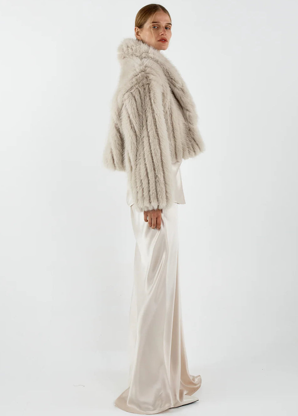 Woman wearing a fur coat and white pants on a white background