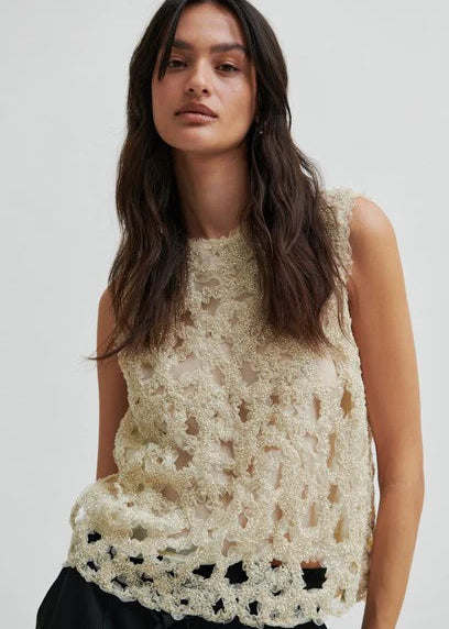 Woman wearing a beige beaded sleeveless top against a white background