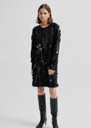 Woman wearing a black sequin dress with knee-high boots on a white background