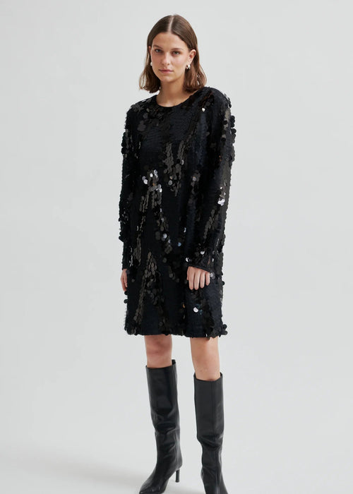 Woman wearing a black sequin dress with knee-high boots on a white background